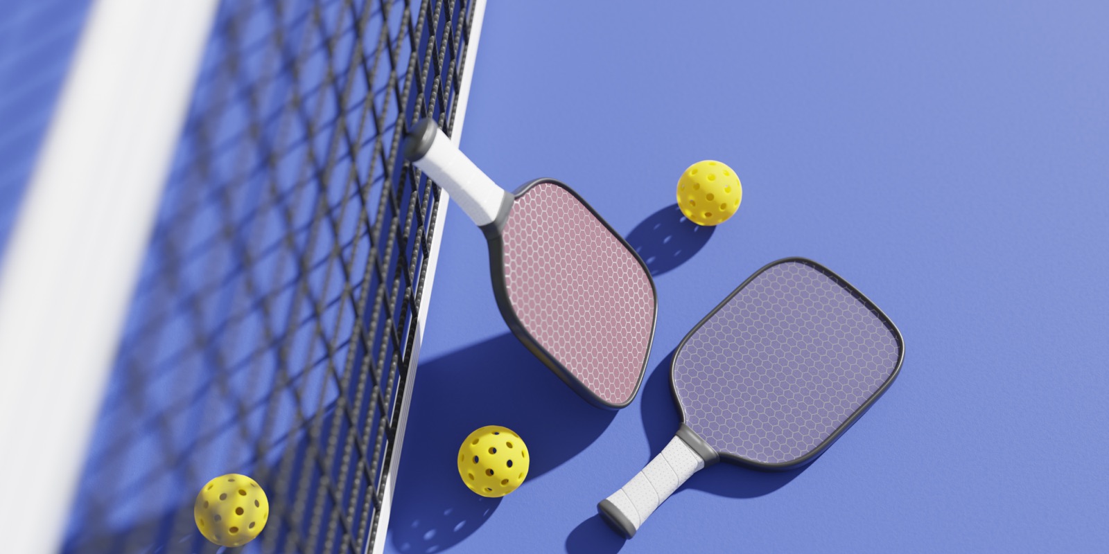 Two pickleball paddles and balls beside the net on a blue court