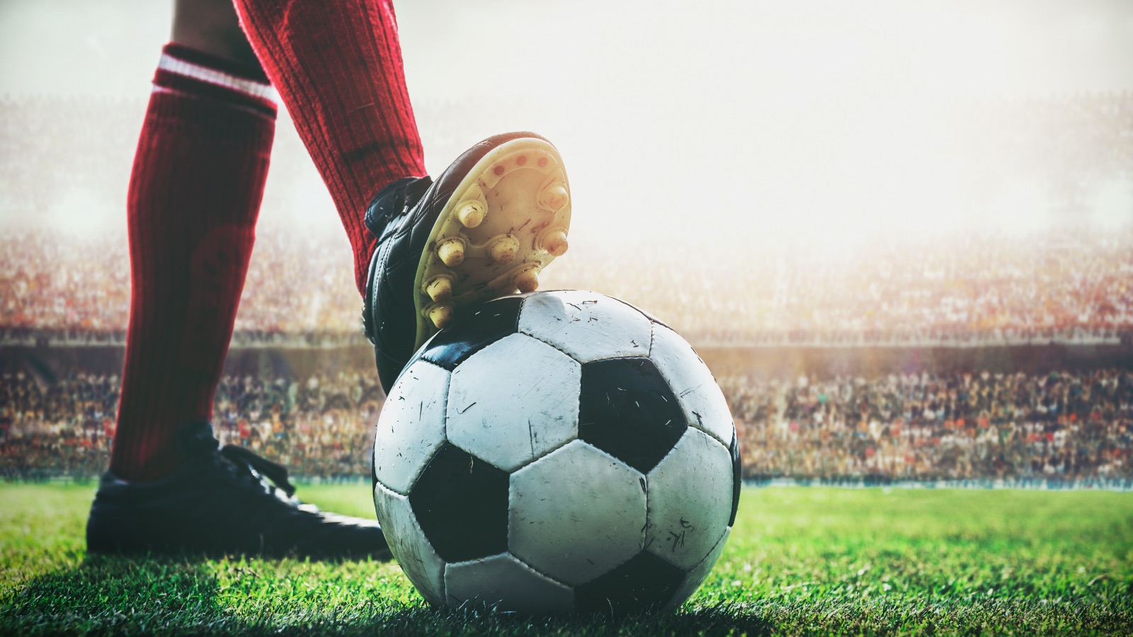 A soccer player in red socks with a boot on the ball in a packed stadium